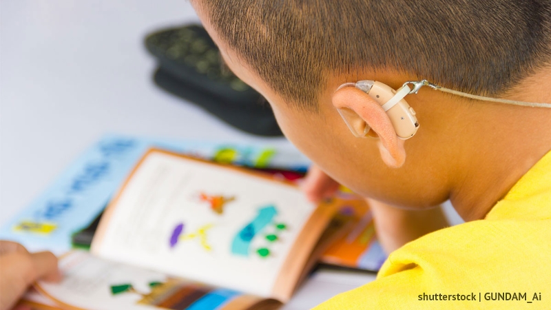 Photo of a child with a hearing aid reading a book. Attribution: Shutterstock | GUNDAM_Ai