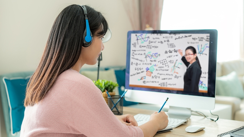 A student watching an instructor on a computer screen surrounded by math concepts